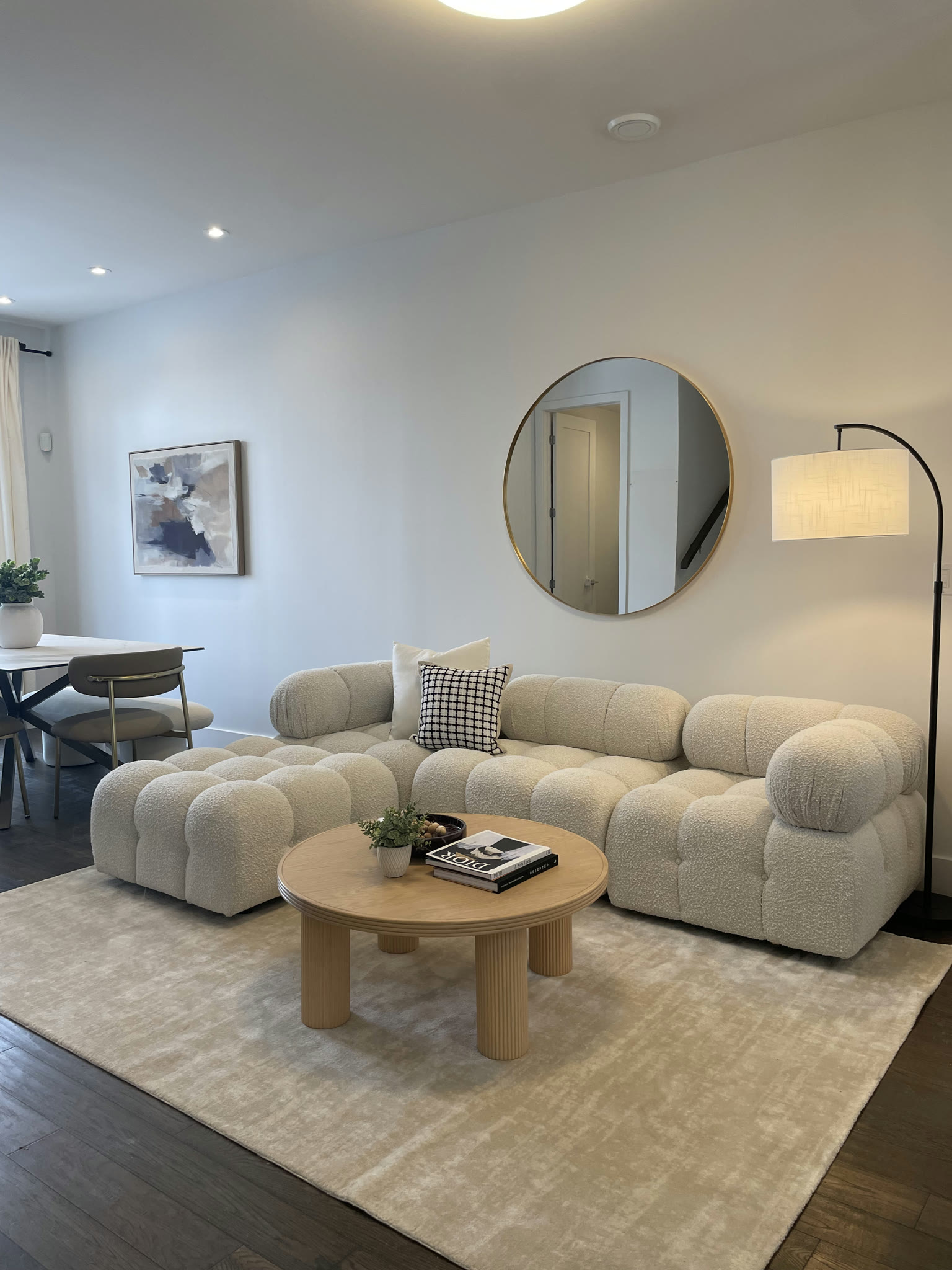 Warm finished living room with a cream sectional, round wood coffee table, floor lamp, and dining area